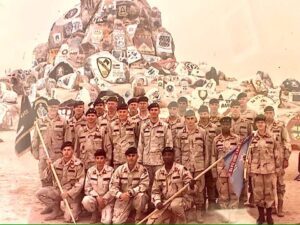 A platoon of soldiers posing for a group photo in front of a rock painted with unit symbols.