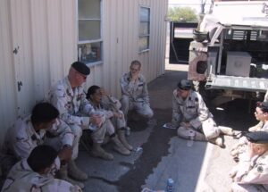 Group of soldiers in desert camouflage uniforms relaxing in the shade next to a building