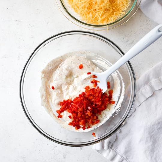 Chopped pimentos added to the mixed cream cheese and mayonnaise base in a clear glass bowl for pimento cheese.