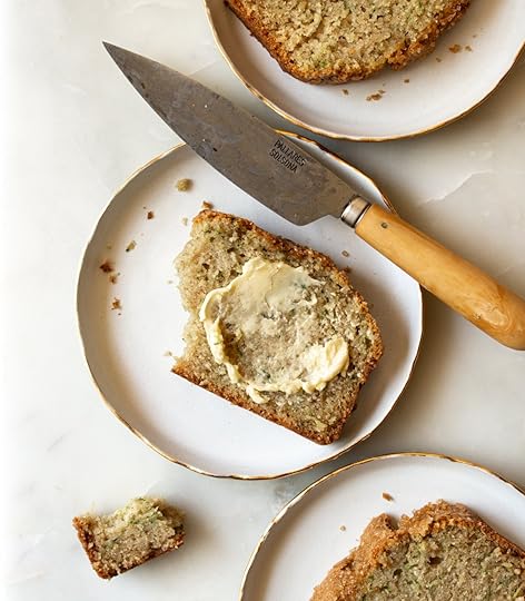 Overhead shot of a buttered slice of moist brown butter zucchini bread on a small white plate with a gold rim, next to a vintage knife and other bread slices.