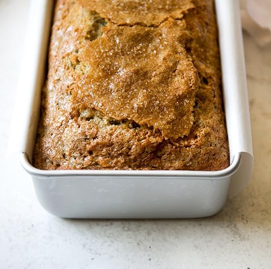 Close-up of a golden brown, crinkly-topped brown butter zucchini bread cooling in a white metal loaf pan.