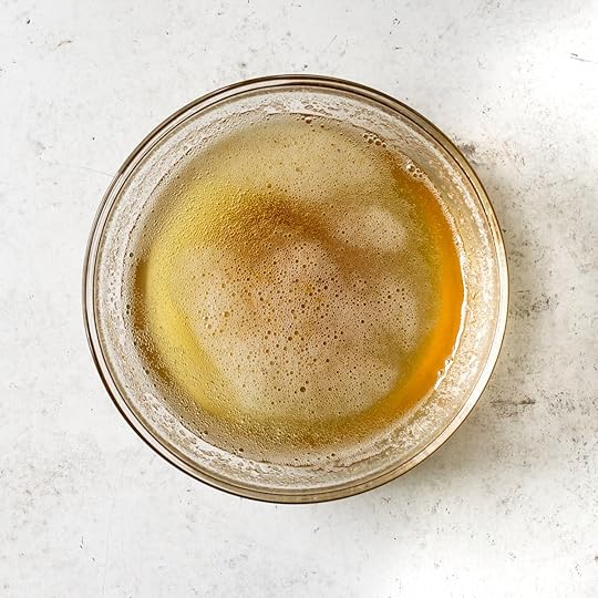 A clear glass bowl filled with golden brown butter, showing foamy edges and browned milk solids at the bottom.