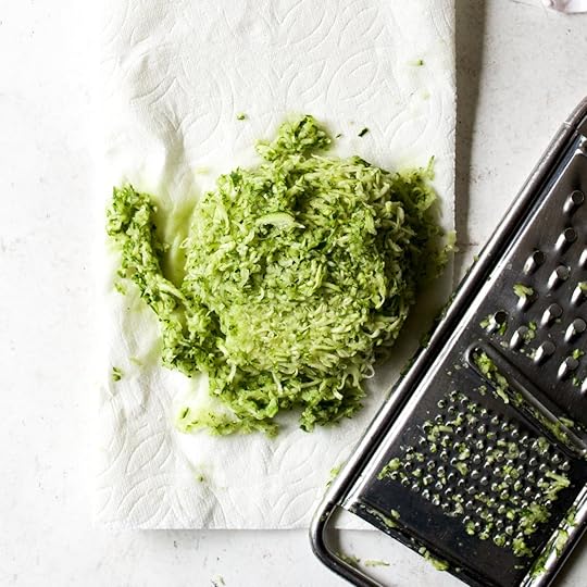 A pile of freshly grated zucchini on paper towels next to a metal box grater, ready for zucchini bread.
