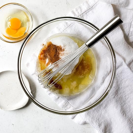 Ingredients in a glass mixing bowl for brown butter zucchini bread, including brown butter, sugar, and spices with a whisk.