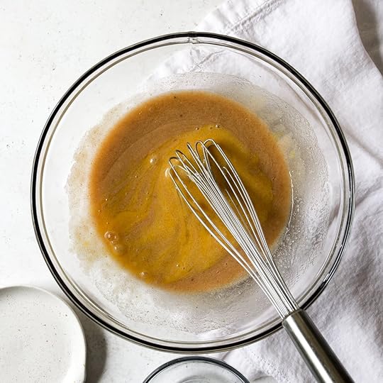 Wet ingredients for brown butter zucchini bread mixed in a glass bowl with a whisk.
