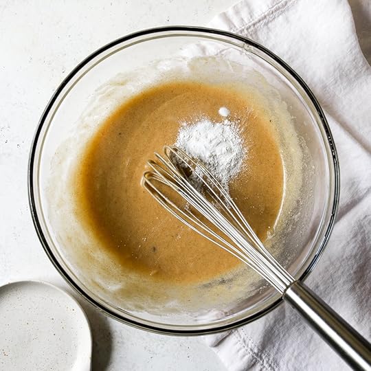 Baking powder, baking soda and salt being added to wet ingredients for brown butter zucchini bread in a glass bowl with a whisk.