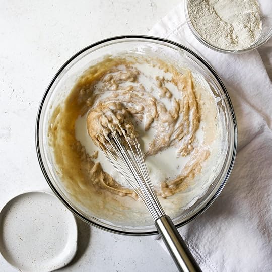 Whole milk being mixed into brown butter zucchini bread batter in a glass bowl with a whisk.