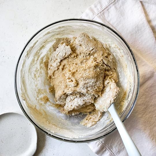 Zucchini bread batter partially mixed with flour in a glass bowl with a white spatula.