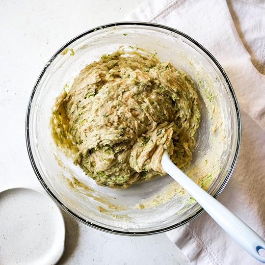 Fully mixed brown butter zucchini bread batter with green zucchini flecks in a glass bowl with a white spatula.