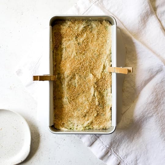 Overhead view of brown butter zucchini bread batter in a white loaf pan lined with parchment paper held by clothespins, with a generous sprinkle of Demerara sugar on top.