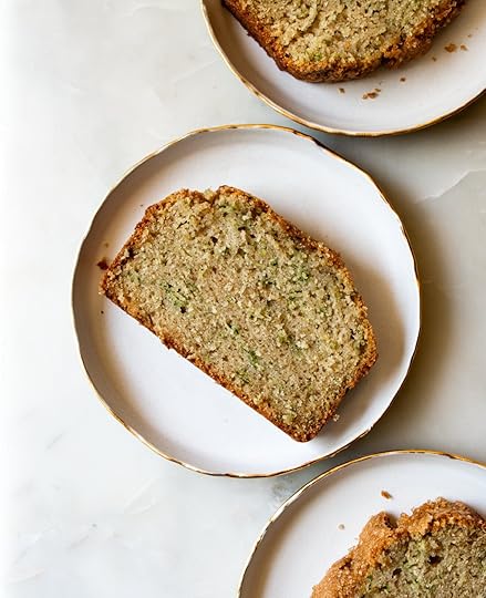 verhead view of a thick slice of homemade zucchini bread, showing green flecks and a tender crumb, resting on a white and gold rimmed plate.