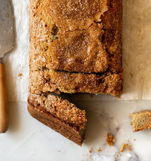 Overhead view of a golden brown, freshly baked zucchini bread loaf on parchment paper, showing a crackly Demerara sugar crust and a few sliced pieces.