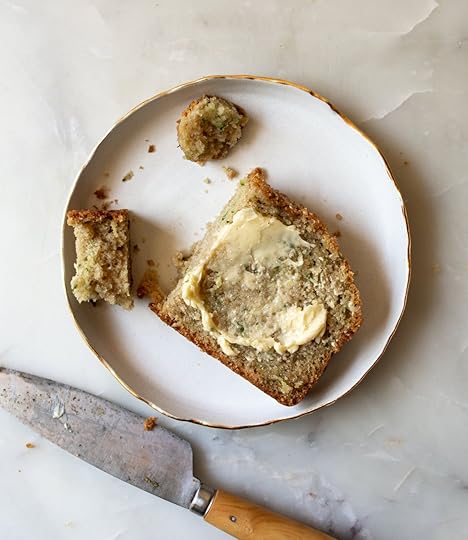 A slice of brown butter zucchini bread with butter on a white plate, with a knife nearby.