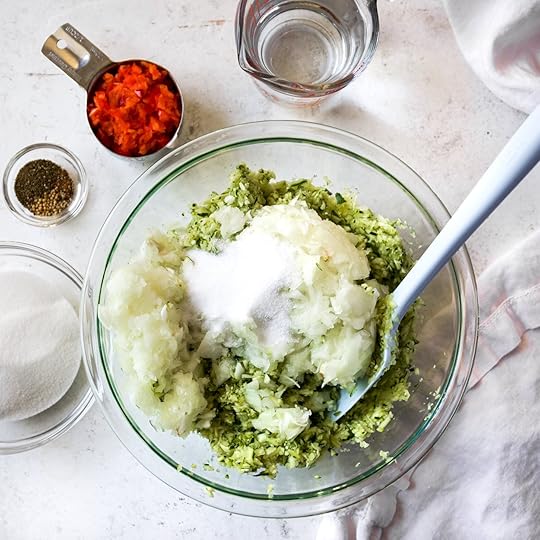 Mixing finely grated zucchini and chopped onions with sugar and spices in a glass bowl, showcasing the initial steps for homemade spiced zucchini relish.