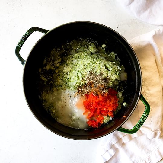 Top-down view of a dark green Staub Dutch oven filled with zucchini, onion, diced red bell pepper, vinegar, and a mix of spices, all combined for making homemade spiced zucchini relish.