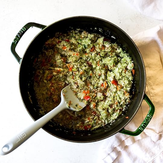 Cooked mixture of finely chopped zucchini, onion, and red pepper, with a spatula, simmering in a green cast iron Dutch oven for homemade spiced zucchini relish.