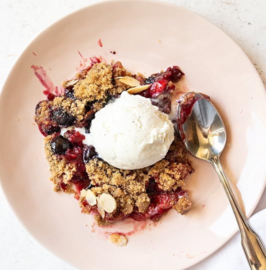 A serving of warm Mixed Berry Crumble with a scoop of melting vanilla ice cream and a spoon on a pink plate.