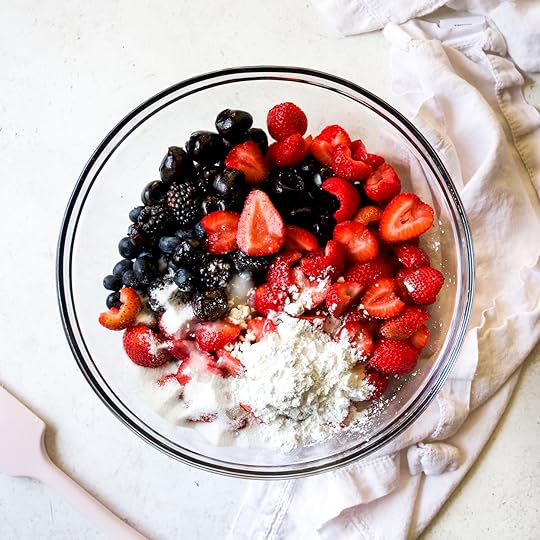 A glass bowl filled with freshmixed berries, including strawberries,blueberries, blackberries, and cherries, with sugar and cornstarch, ready for a homemade crumble.