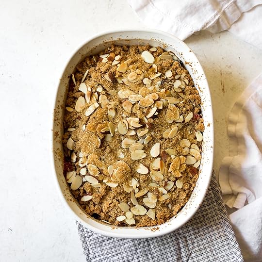 Freshly baked Mixed Berry Crumblein a white oval baking dish,featuring a golden-brown streuseltopping with visible sliced almondsand sparkling Demerara sugar.