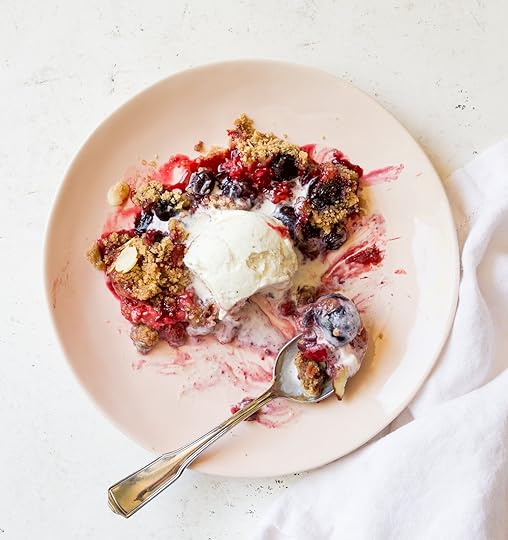 A close-up of a generous serving of warm Mixed Berry Crumble topped with melting vanilla ice cream and a spoon on a light pink plate.