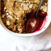 Easy Mixed Berry Crumble with Almond Topping and Demerara Sugar in a white baking dish with a spoon.