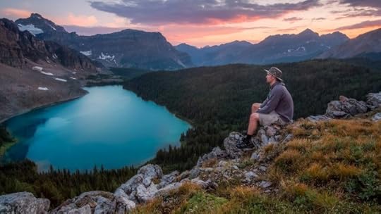 A man in a hat on a hill, overlooking a calm lake. How do you stay aware of the world without becoming overwhelmed?
