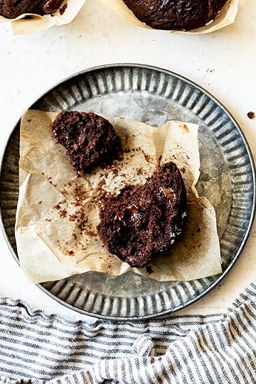 A metal colored plate with light brown parchment paper with a half eaten chocolate zucchini muffin on top.