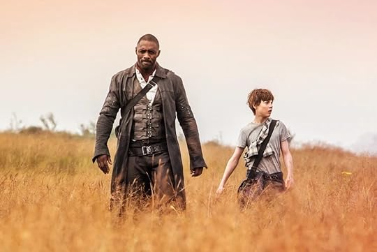 Roland (Idris Elba) wearing a long black duster and Jake Chambers walk through an orange field of wheat with a sienna-tinged sky in the background. 