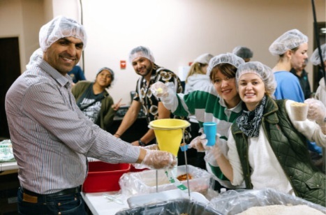 A group of volunteers working together to prepare and package food in a community service setting, wearing hairnets and gloves.