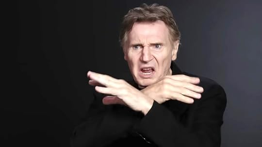 Lian Neeson with his hands folded doing a flying motion and making a strange face