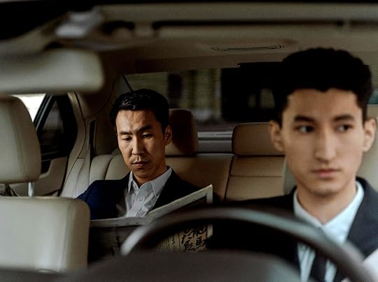 Two Asian men in a car with a cream interior, one reading a newspaper
