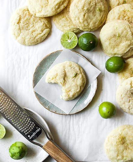 Soft, pillowy key lime cookie with a bite taken out on a plate, surrounded by fresh key limes and a microplane zester.