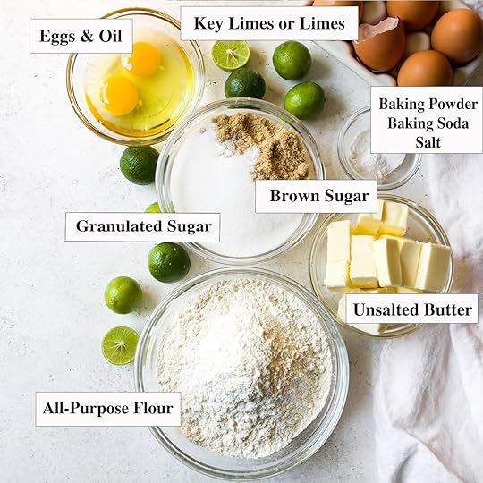 Flat lay photo showing all the ingredients for a key lime cookie recipe, including labeled bowls of flour, butter, sugar, eggs, and fresh key limes.