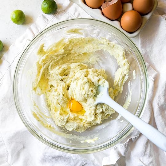 A cracked egg being added to a bowl of creamed butter, sugar, and key lime zest cookie dough, showing a step in the key lime cookie recipe.