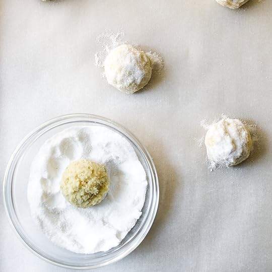 A ball of key lime cookie dough being rolled in a bowl of granulated sugar before baking.