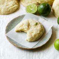 Soft pillowy key lime cookie with a bite missing on a plate with fresh key limes.