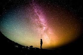 A silhouette of a person standing against a vibrant night sky filled with stars and the Milky Way, showcasing a rich blend of colors from purple to orange.