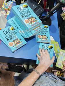 Debbies hands putting bookmarks into signed copies of Death at the Old Curiosity Shop in Newport