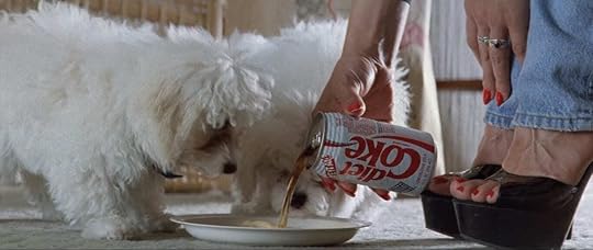 Two small white dogs drink from a dish of Diet Coke, poured by a woman with red fingernails, a red pedicure, and black peep-toe heels in