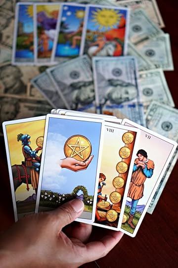 Hand holding tarot cards with pentacles imagery, laid over US dollar bills and additional tarot cards in the background, symbolizing affirmations for money and financial manifestation.