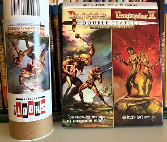 Slipcase 4K Blu-ray. The art is split in half vertically. The left side is poster for Deathstalker 1 and the right side is the poster for Deathstalker 2.To the right is an upside down cardboard tube holding a poster.