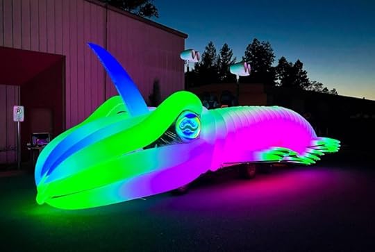 A cuttlefish-shaped art car glows shockingly blue, green, and purple at dusk.