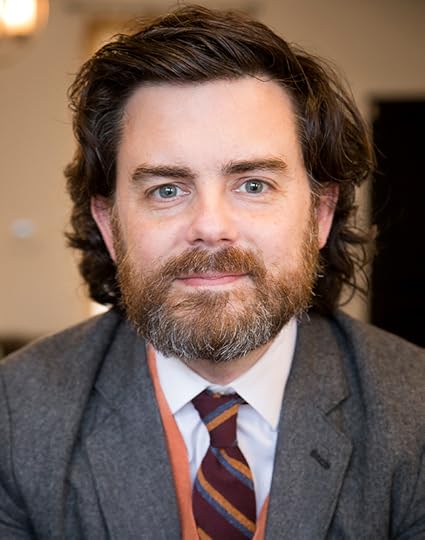 Head-and-shoulders color portrait of Clay Risen facing the camera. He is wearing a suit and tie, has a beard and dark brown hair.
