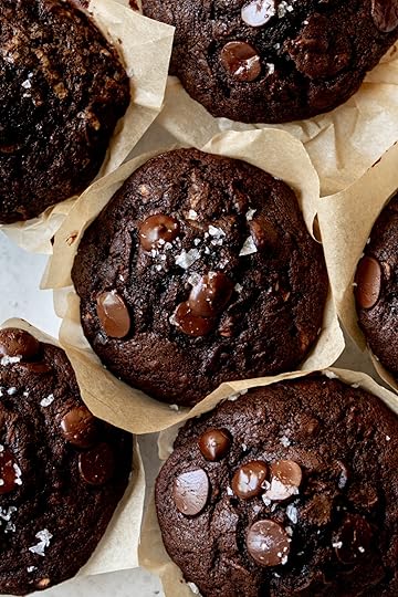 A close-up overhead shot of rich, bakery-style double chocolate zucchini muffins. The dark, moist muffins are topped with melted chocolate chips and a sprinkle of flaky sea salt and are sitting in rustic parchment paper liners.