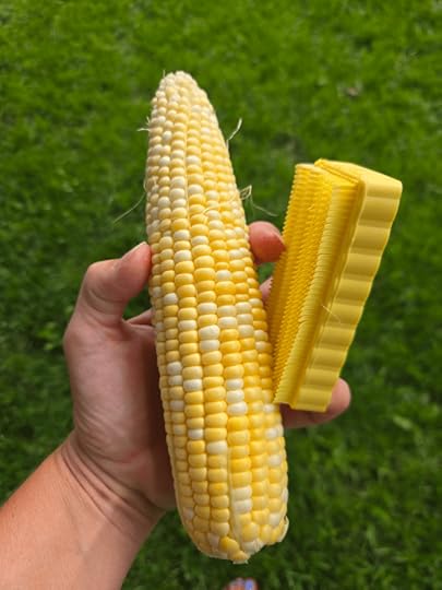A cob of corn and a de-silking brush being held up in one hand