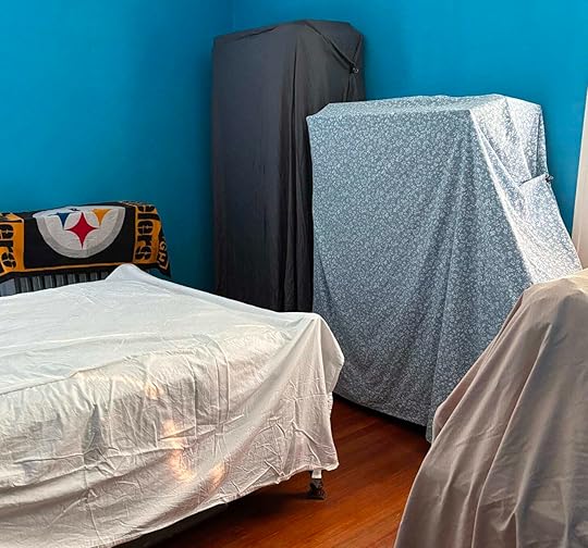 A room with blue walls, furniture covered with odd sheets and towels.