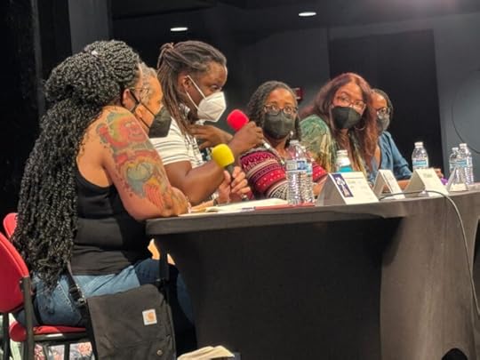 Six panelists at a table seen from the side. All six are Black or mixed race. Pictured are LD Lewis (Moderator), Christopher Caldwell, LP Kindred, Rebecca Roanhorse, Erin Roberts, and Nicole Glover.
