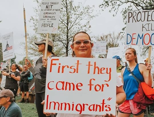 Protesters hold signs about immigrants and democracy.