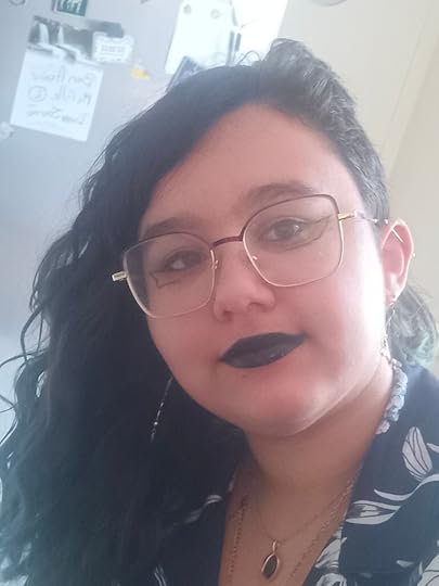 A young mixed French-Indian woman with wavy brown and blue hair, brown skin and eyes, dark lipstick and make-up, and a shirt with flowers on it.