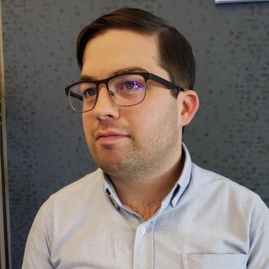 Photo of Alex Tunney wearing a button-down shirt and glasses, gazing to the person's right.